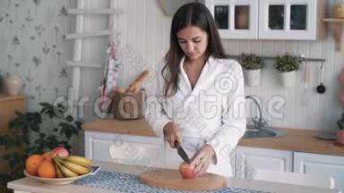 穿着浴袍的可爱女孩拿着苹果，放在船上，切在厨房里，慢动作